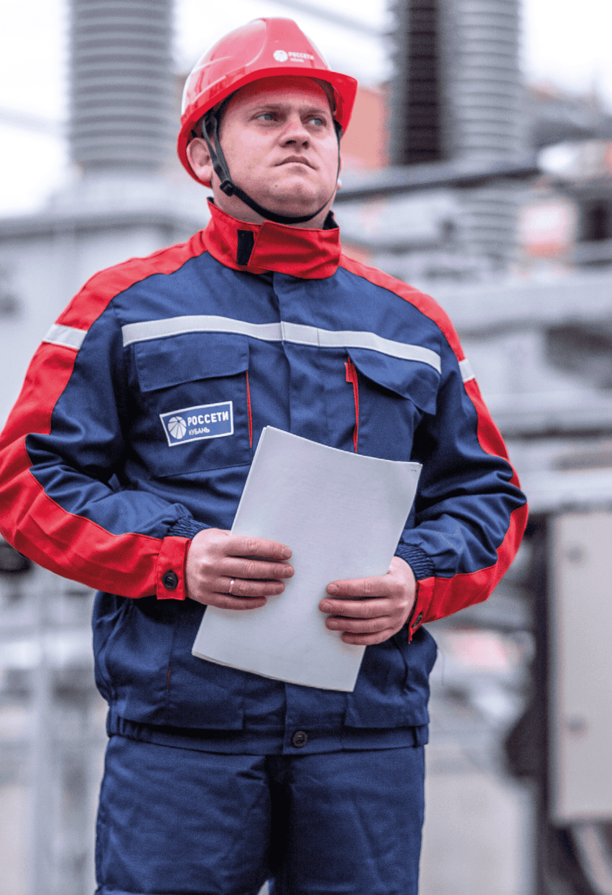 Рабочий в каске с документами в формате листов А4 на фоне электростанции