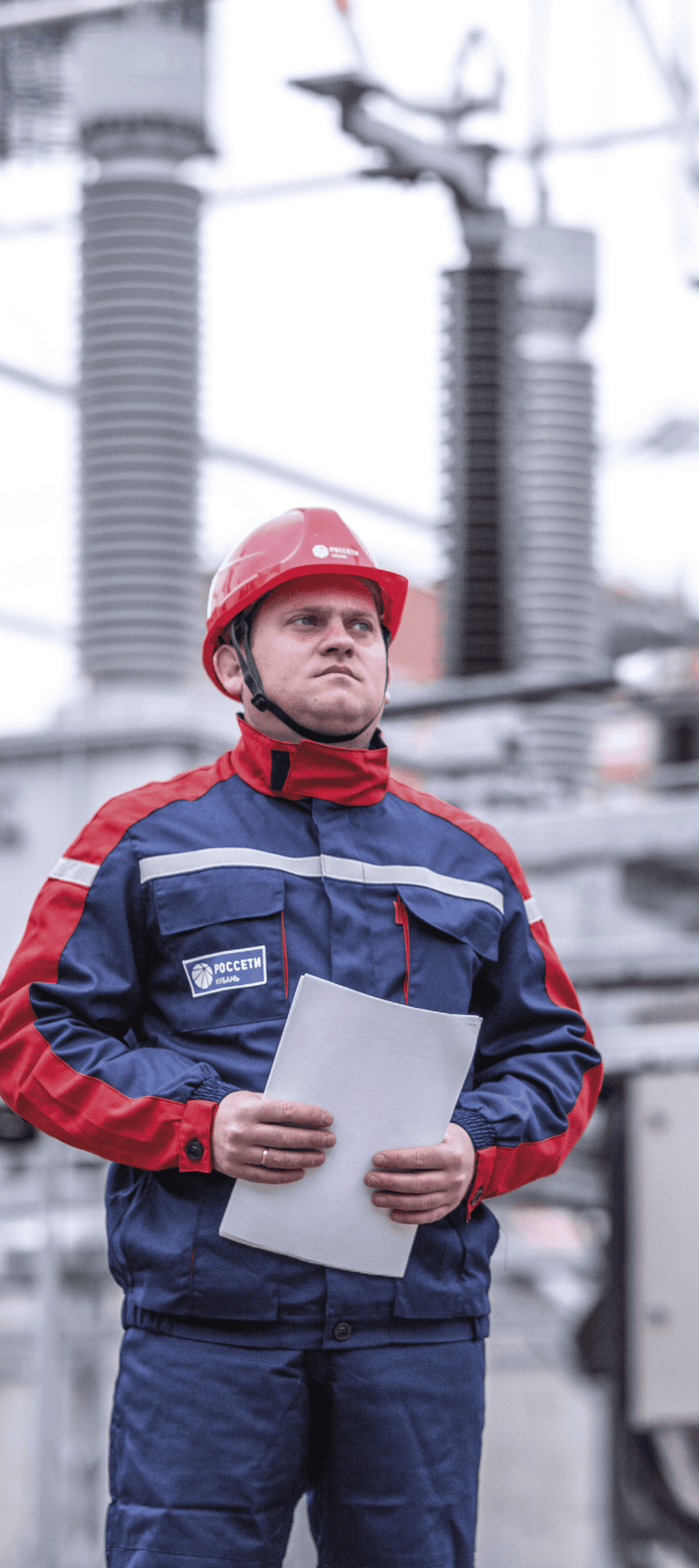 Рабочий в каске с документами в формате листов А4 на фоне электростанции